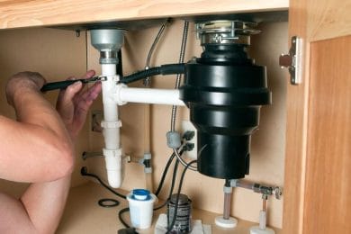 Plumber repairing a garbage disposal beneath a kitchen sink in Wildwood